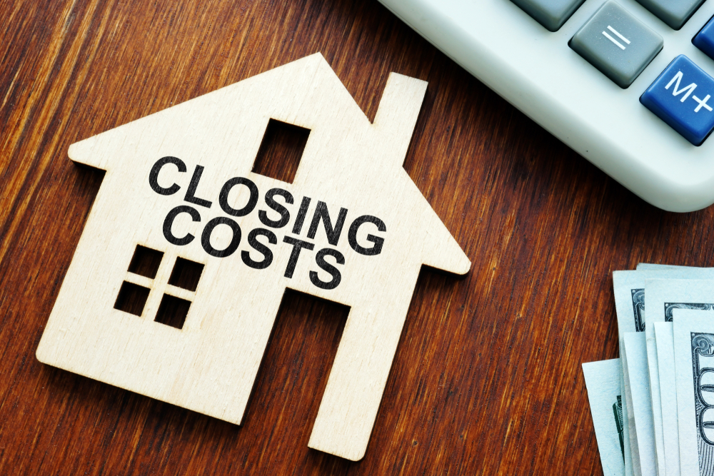 Closing costs in real estate shown with house model, calculator, and cash at closing table